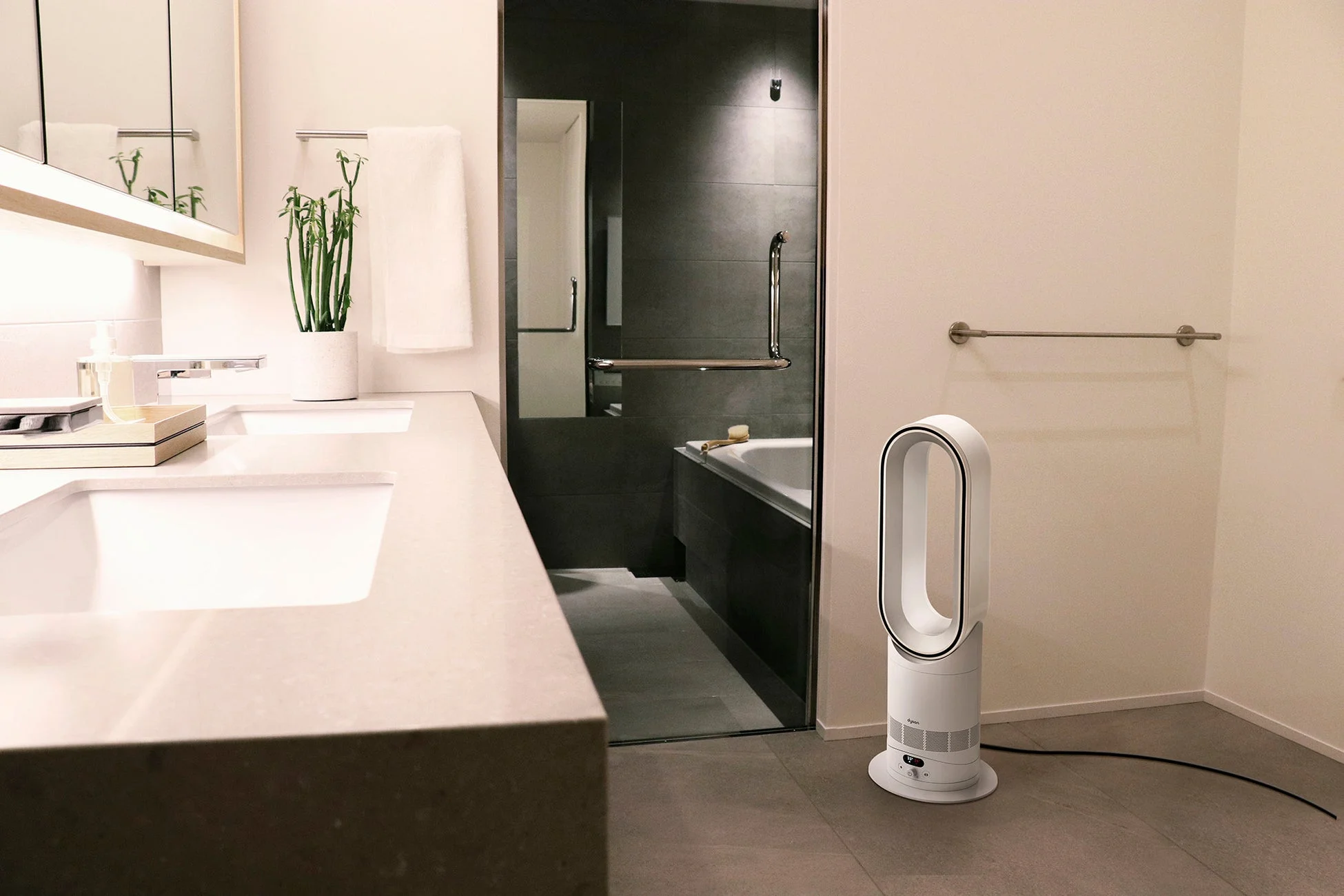 モダンでスタイリッシュなバスルームの全景。二連シンクとシャワールームが見え、床にはダイソンの空気清浄ファンヒーターが置かれています。