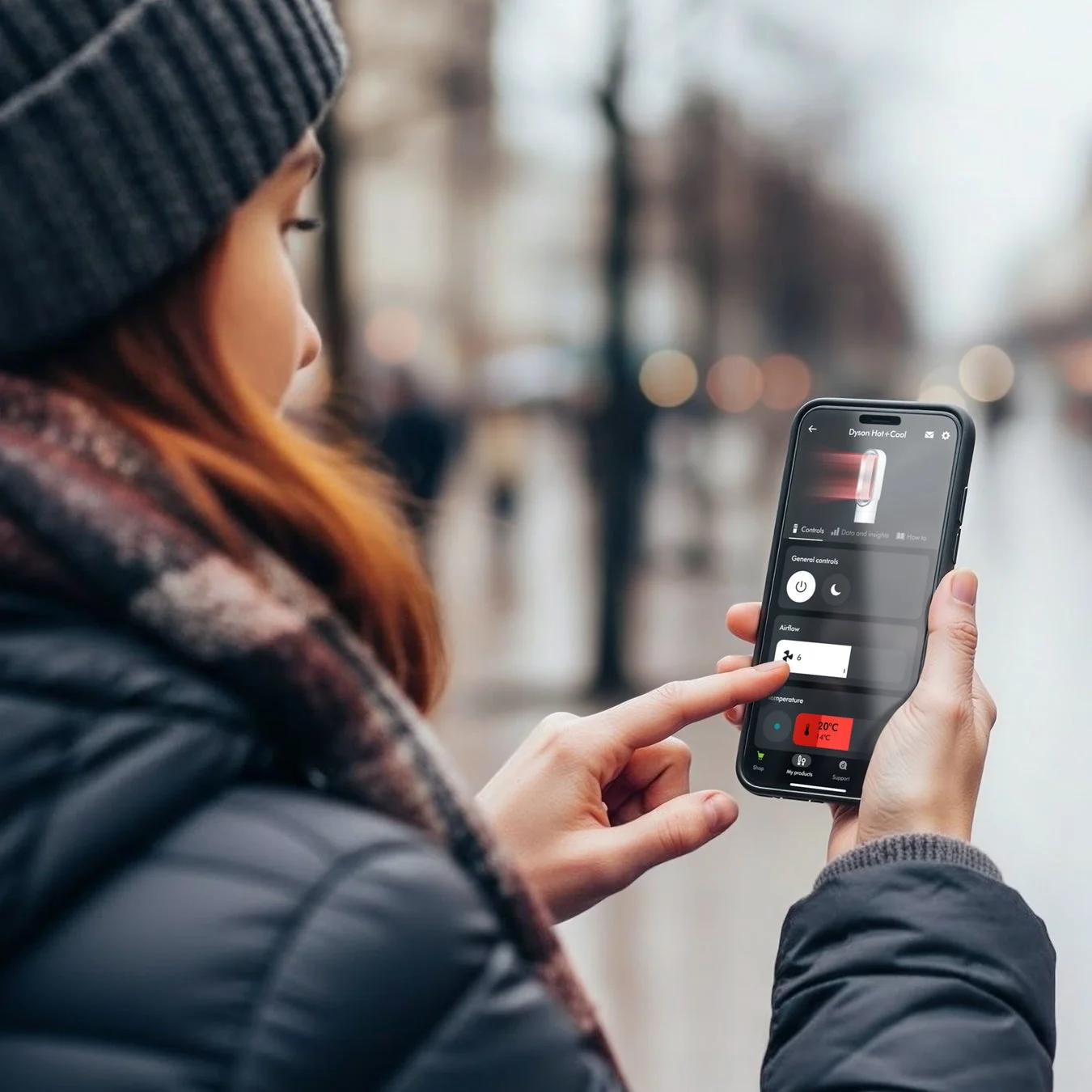 冬の屋外で、女性がスマートフォンを操作しDyson Hot+Coolのアプリ画面を見ている。