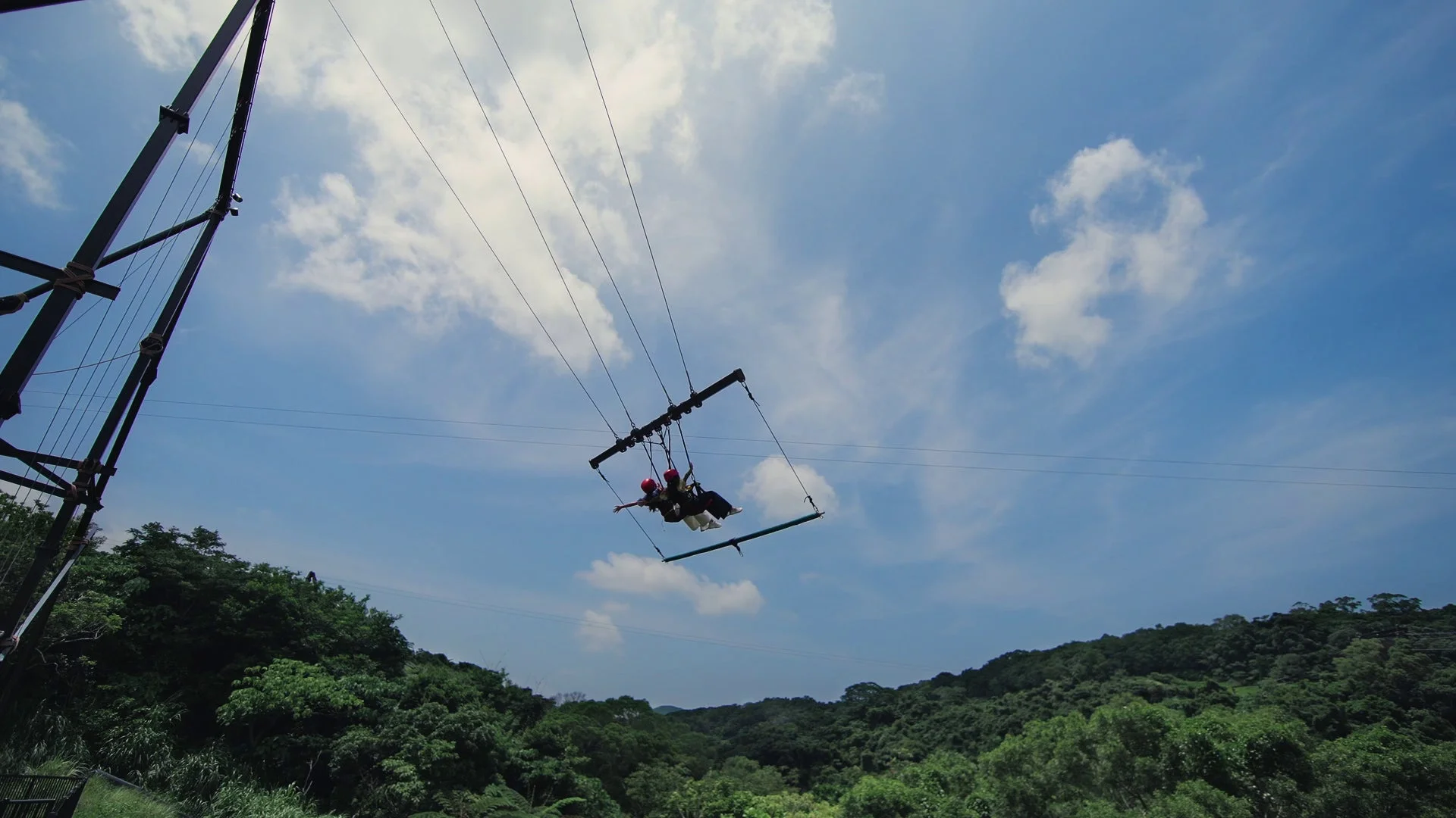 青空と豊かな森を背景に、二人が空中アトラクションで楽しんでいる様子
