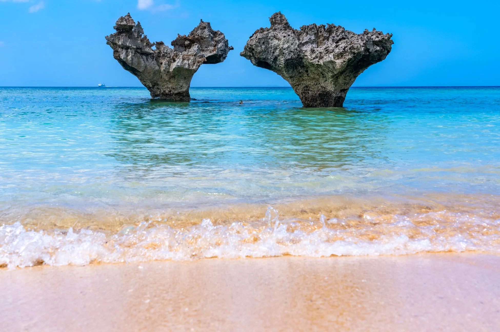 澄み切った青い海と白い砂浜が広がるビーチに、特徴的なハート型の岩