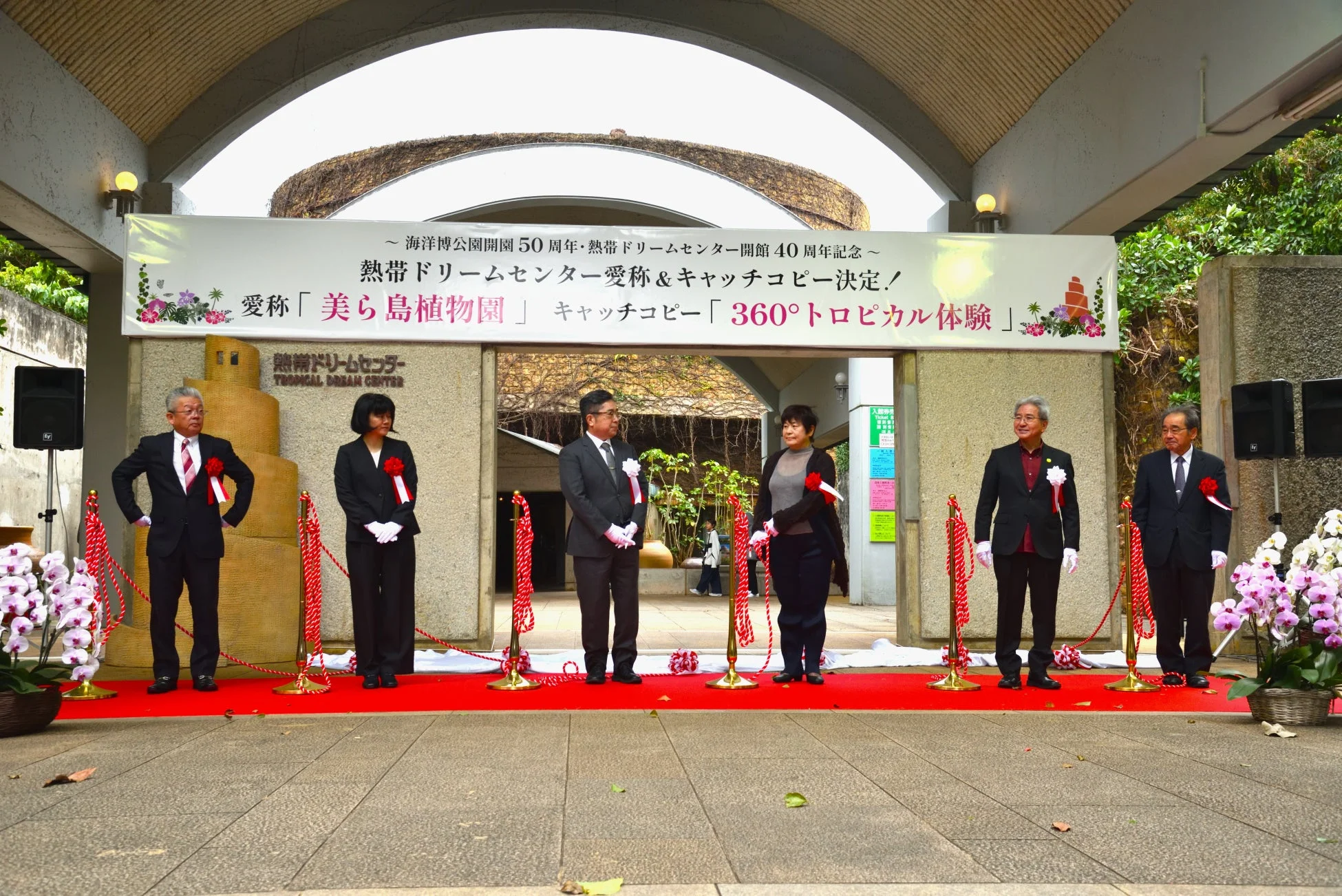 海洋博公園開園50周年と熱帯ドリームセンター開館40周年を記念し、愛称「美ら島植物園」とキャッチコピー「360°トロピカル体験」を発表する式典の様子。赤いカーペットの上で関係者らしき人々が並んでいます。