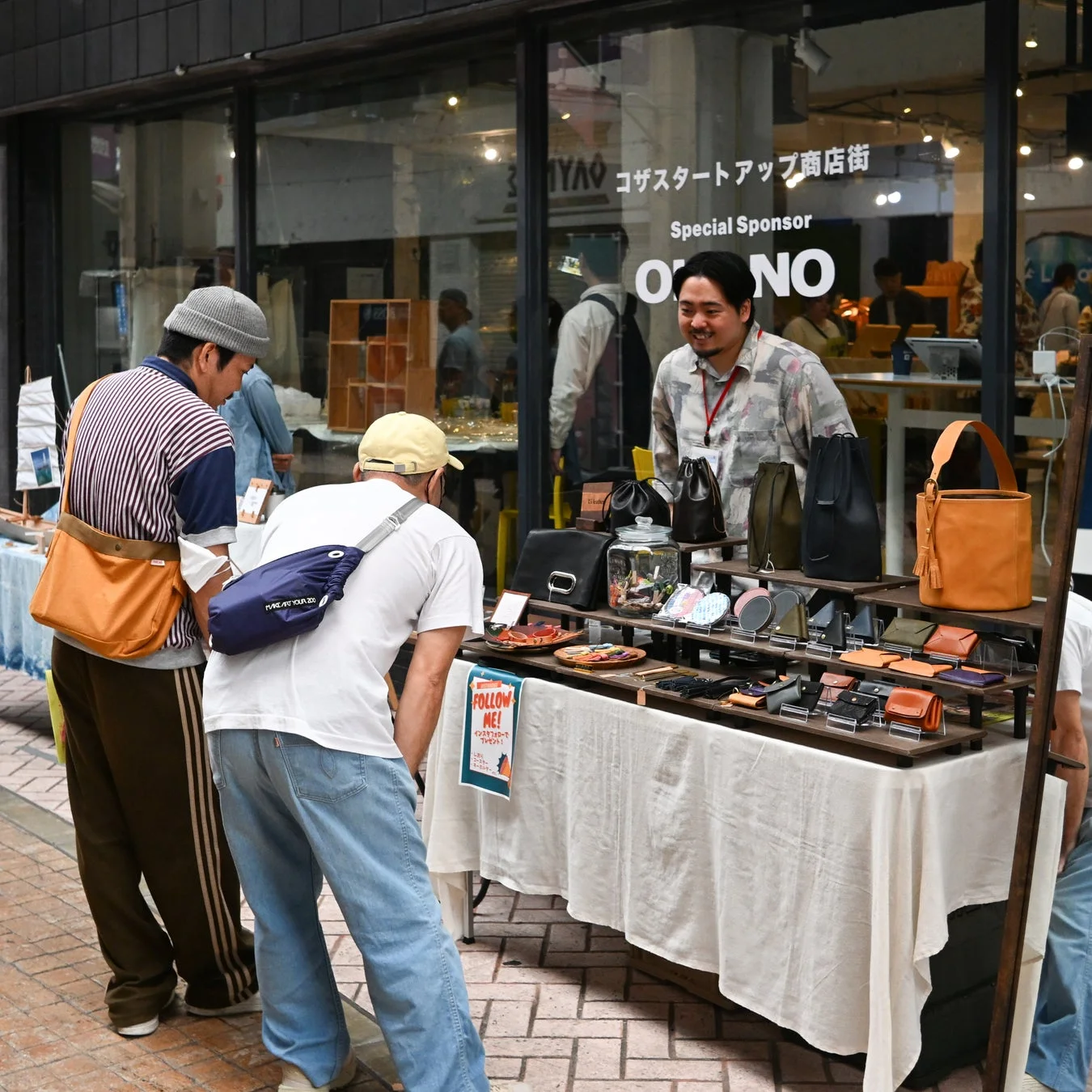 商店街の屋外イベントで革製品のブースを見て交流