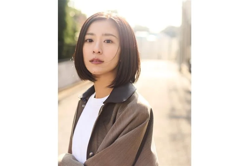 ボブヘアの女性がカジュアルなジャケットを着用し、屋外でカメラを見つめているポートレート写真です。自然光が当たり、柔らかな雰囲気です。