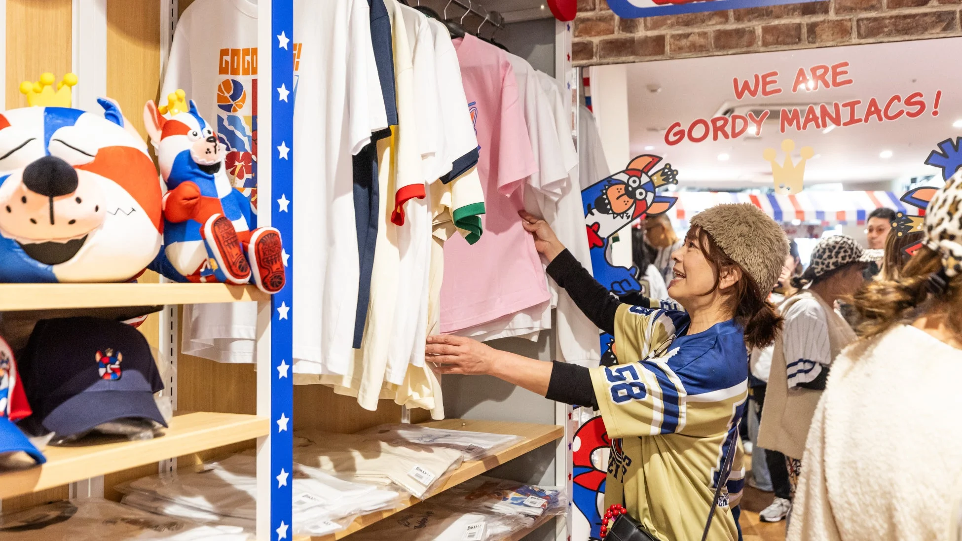 女性がファンショップで楽しそうにTシャツなどのグッズを選んでいます