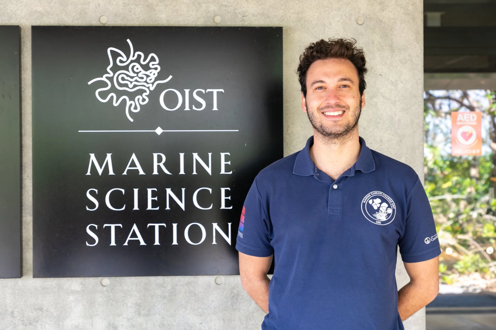 OIST海洋科学ステーションの看板前で立つルカス・フランカ・フルタード氏