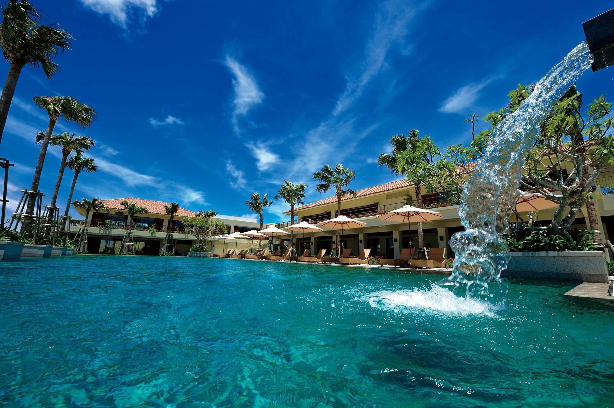 青い空の下、ヤシの木が並ぶ豪華なリゾートホテルのプールサイド