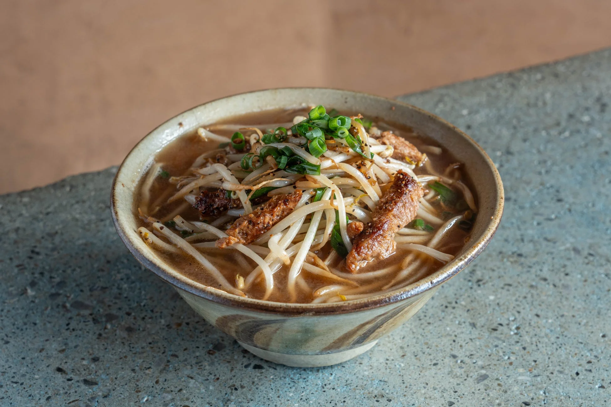 もやしと肉、青ネギがたっぷりトッピングされた温かい麺料理