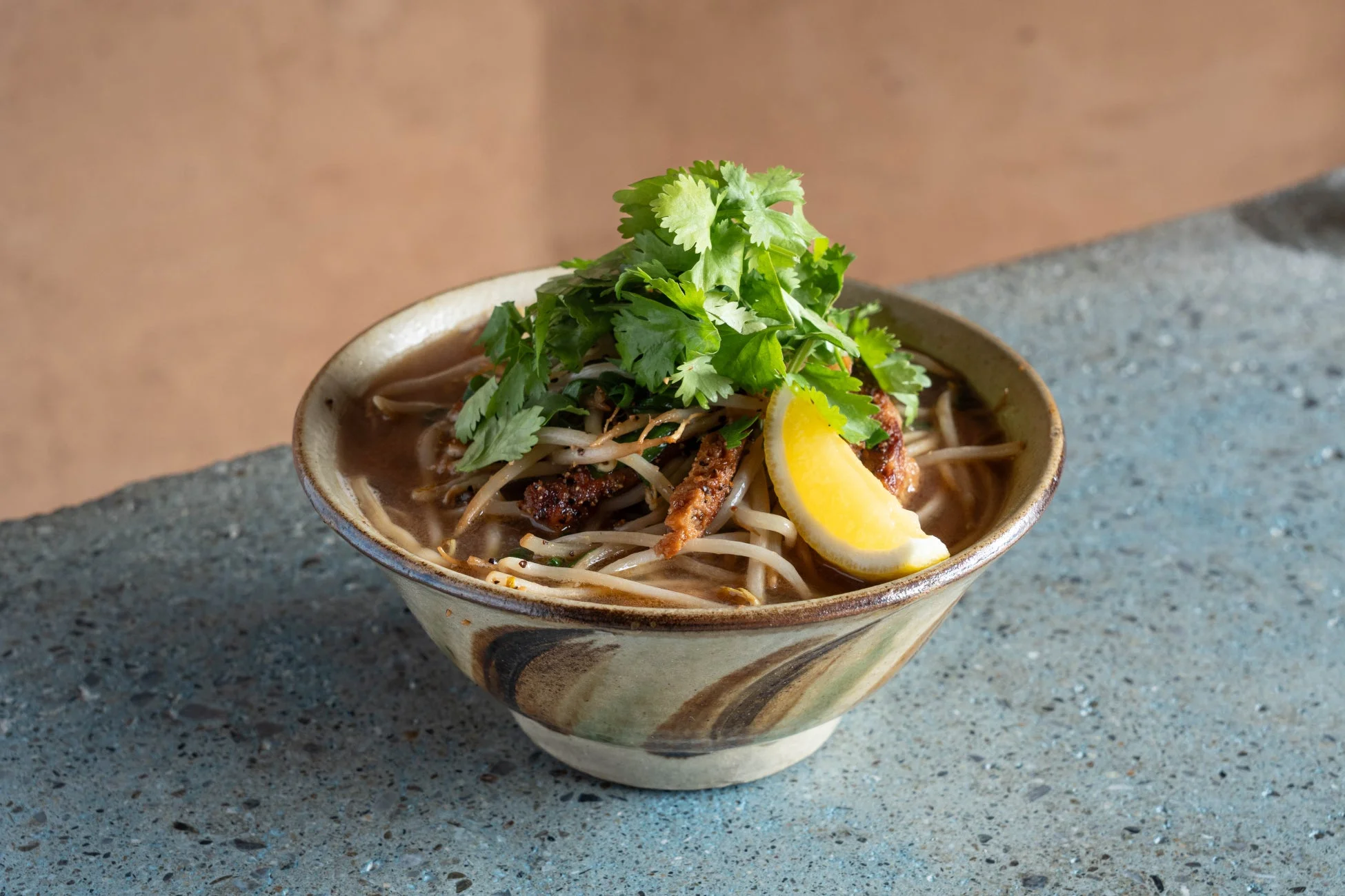 たっぷりのパクチー、もやし、レモンのくし切りが添えられた温かい麺料理