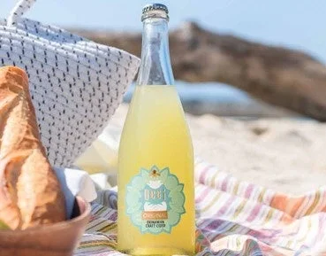 砂浜に敷かれたカラフルなブランケットの上に、BOOCHCRAFTのオリジナルオーガニックハードクラフトサイダーのボトル