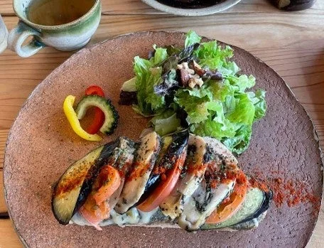 ナスやトマトなどの野菜が層になったメイン料理と、新鮮な葉物野菜のサラダ