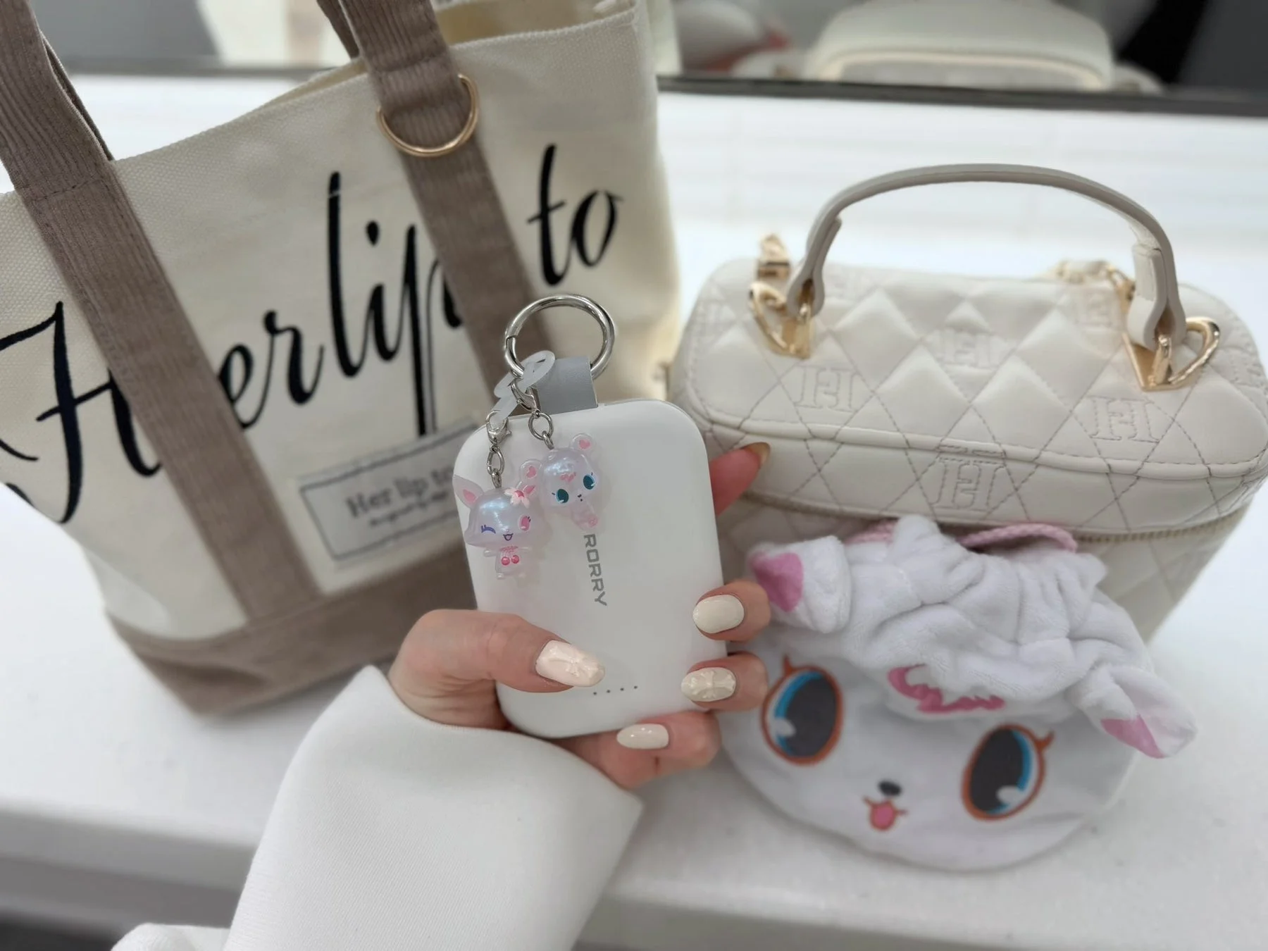 女性の手が白いモバイルバッテリーを持ち、周りにおしゃれな小物