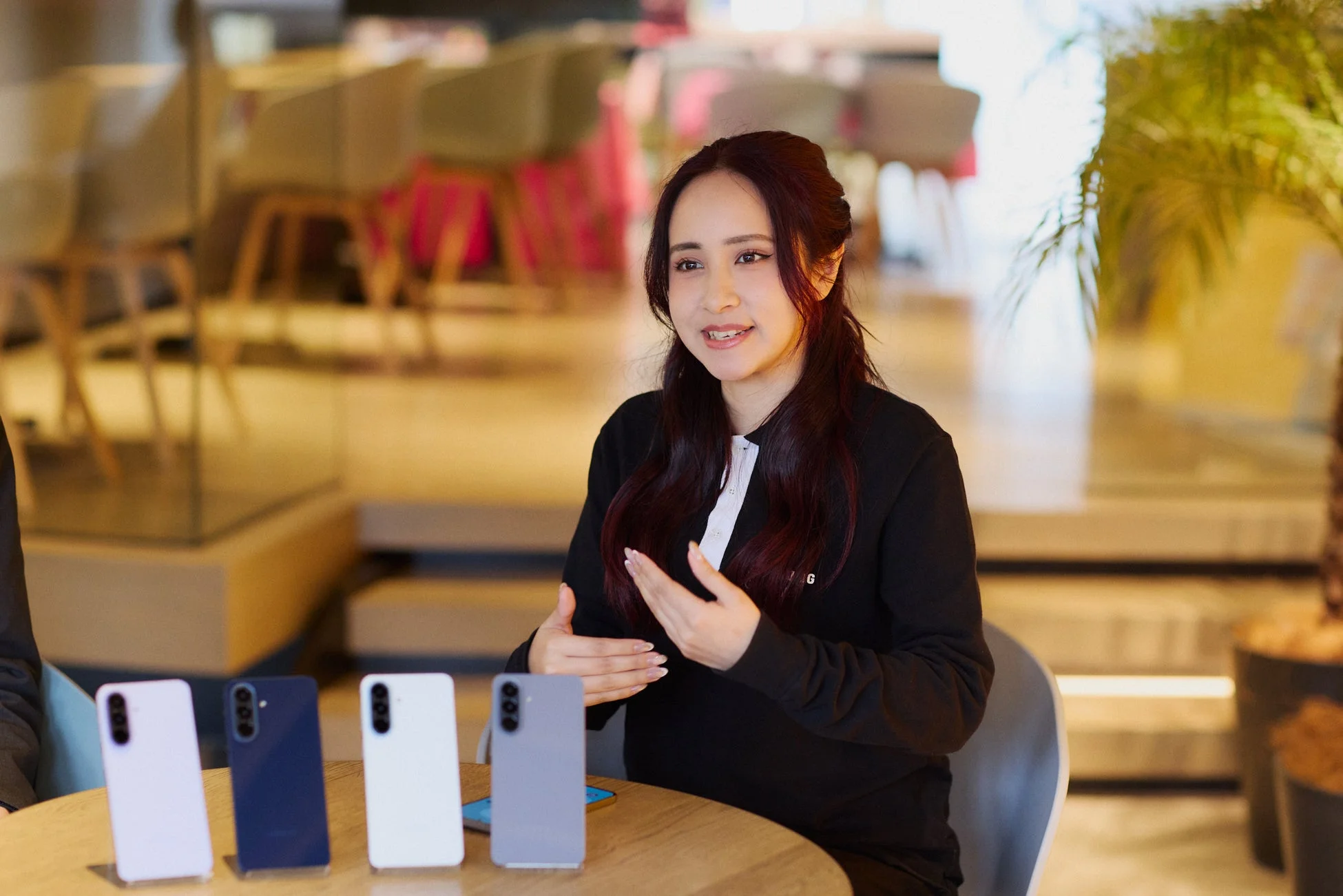 屋内の会場で、一人の女性がスマートフォン製品について説明している様子