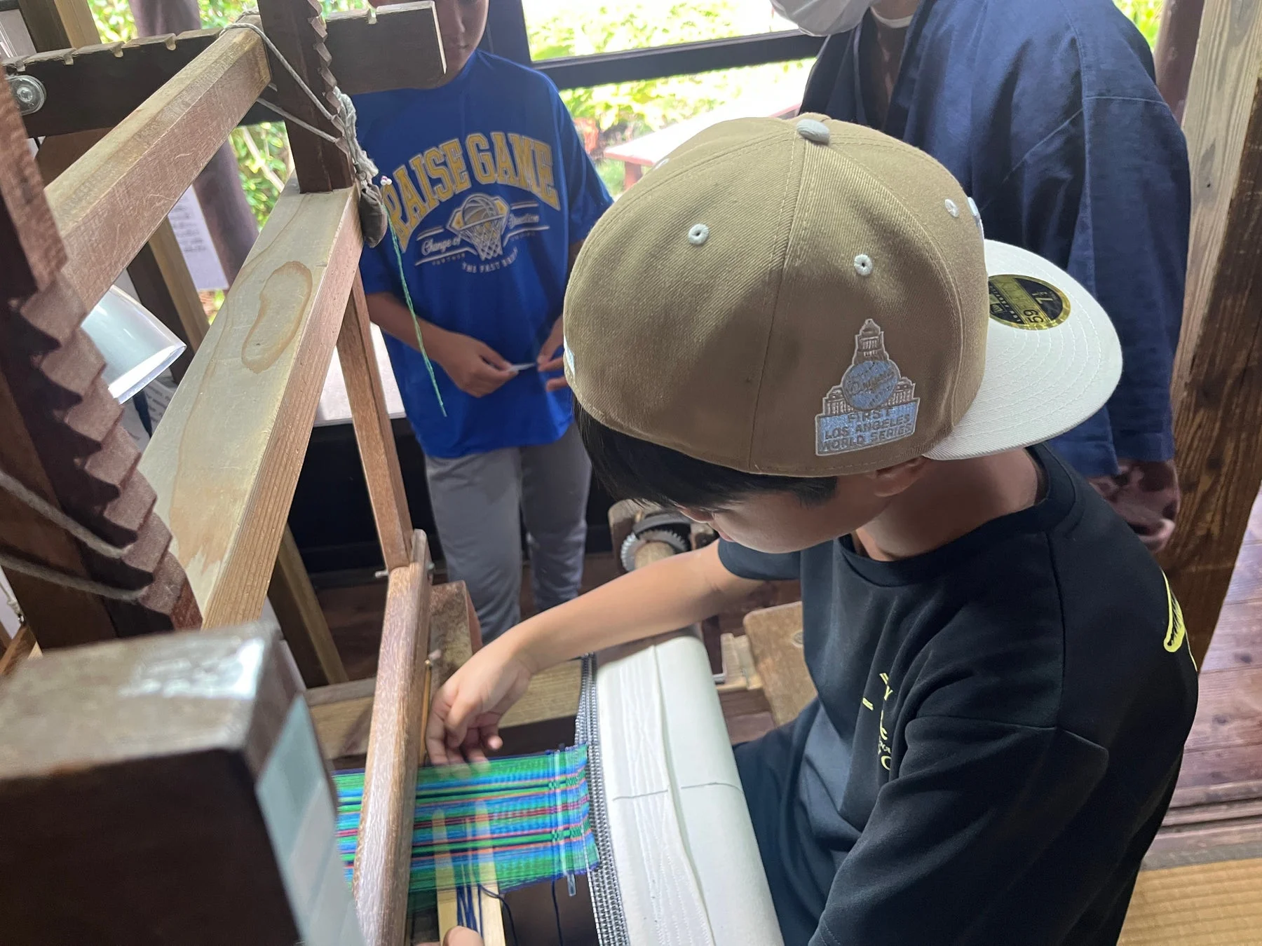 帽子をかぶった子供が機織り機でカラフルな布を織っている様子