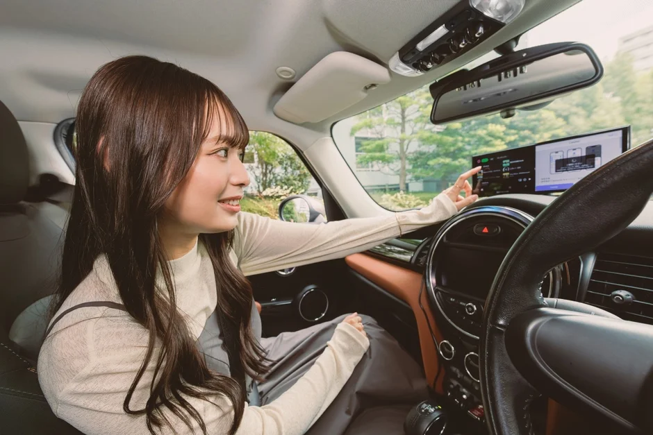 車の運転席でディスプレイを操作する女性、音楽アプリのような画面