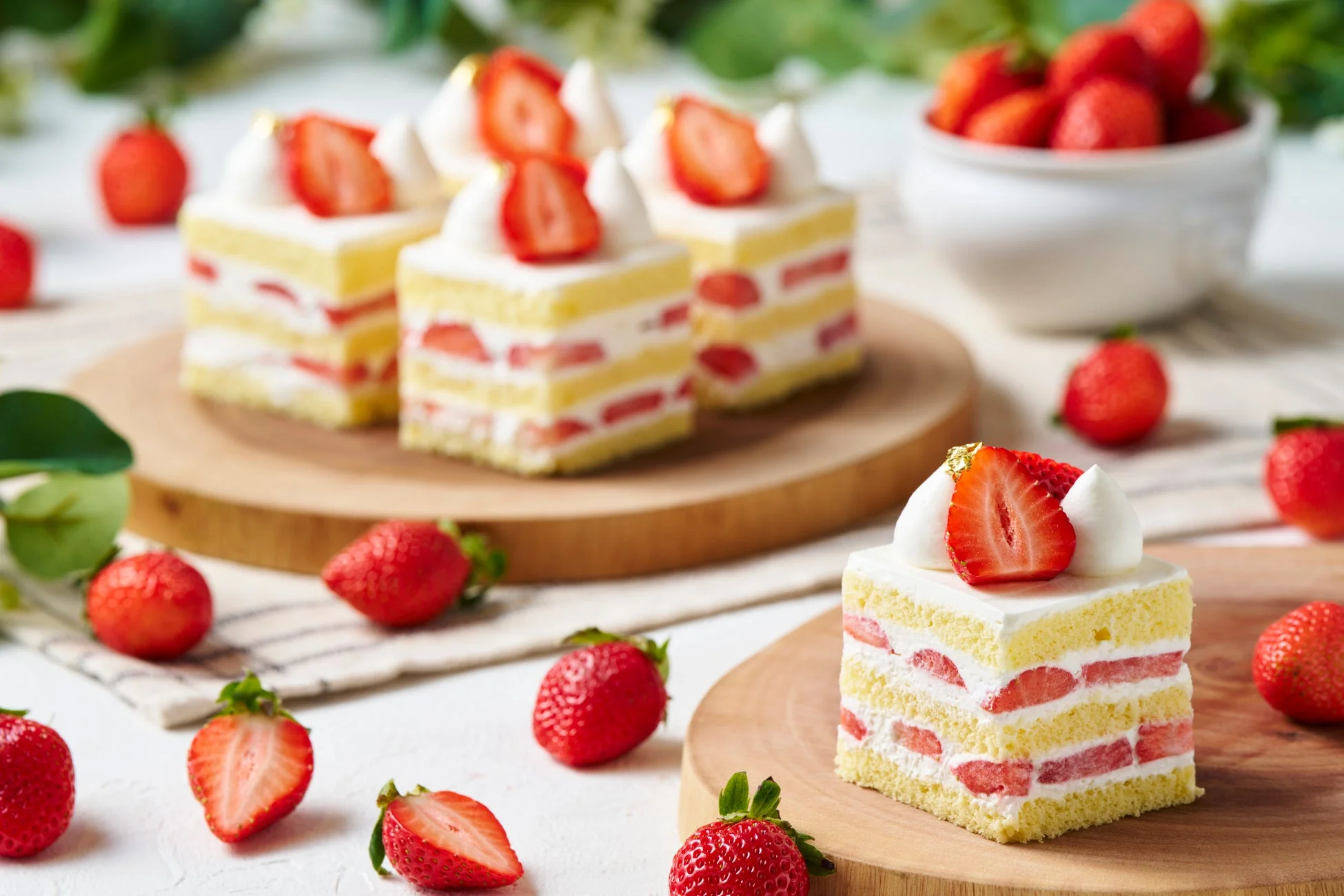 木製ボードに並べられた、いちごのショートケーキの画像です。スポンジ、生クリーム、新鮮ないちごが層になり、周りには生のいちごが散らばっています。美味しそうで華やかなデザートの風景です。