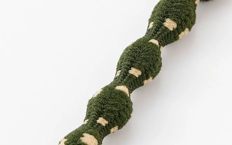 白い背景に、緑色でベージュの斑点模様が入った、でこぼことした質感の太いコードまたはロープがクローズアップで写っています