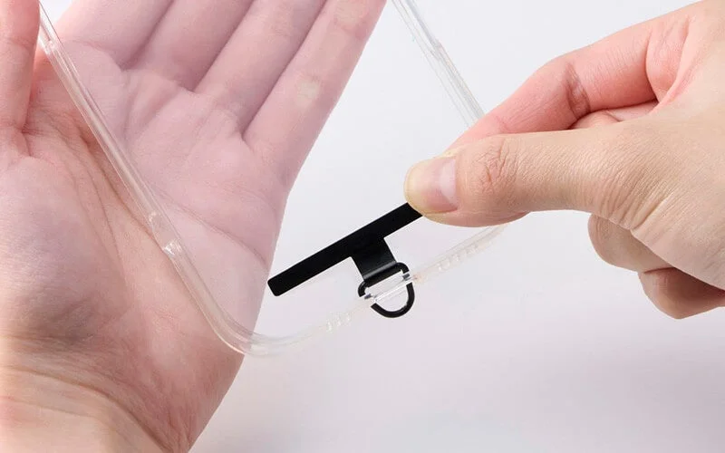 透明なスマートフォンケースの充電ポート部分に、ストラップやショルダーストラップを取り付けるためのDリング付きホルダーを装着している様子