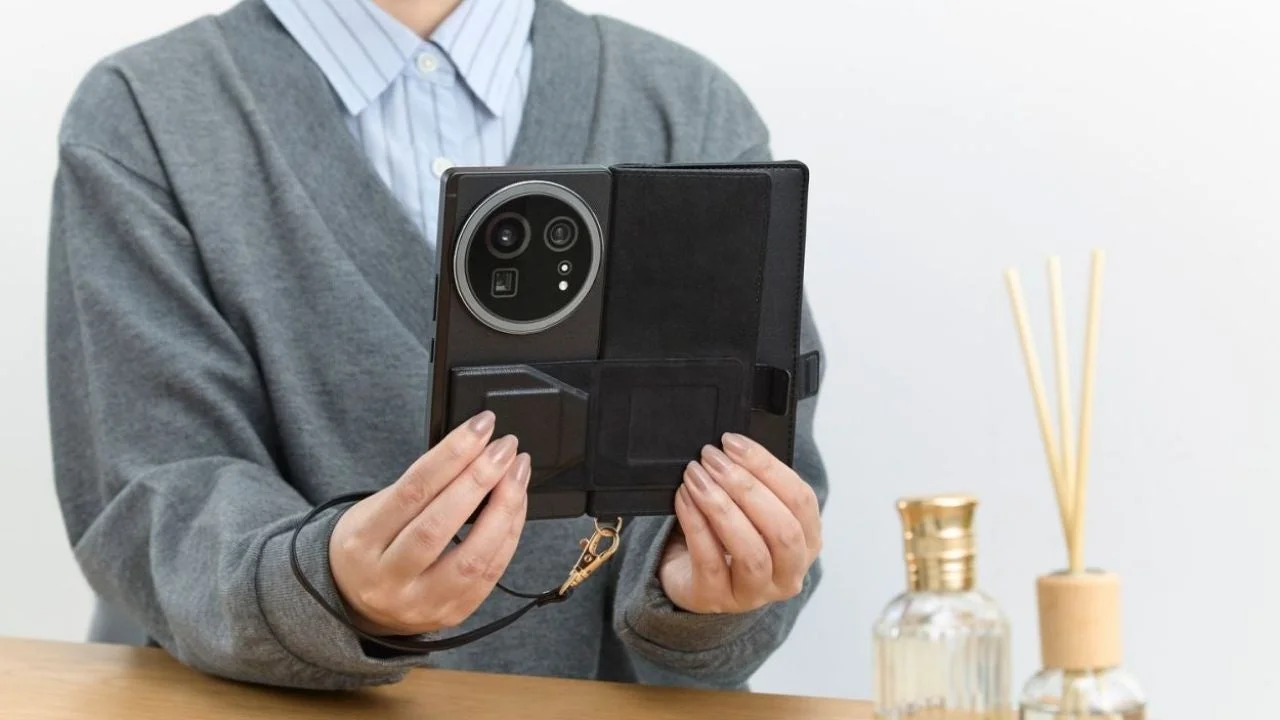 女性が大きなカメラモジュールを持つ黒いスマートフォンを、ストラップ付きのフォリオケースに入れた状態で両手で持っている