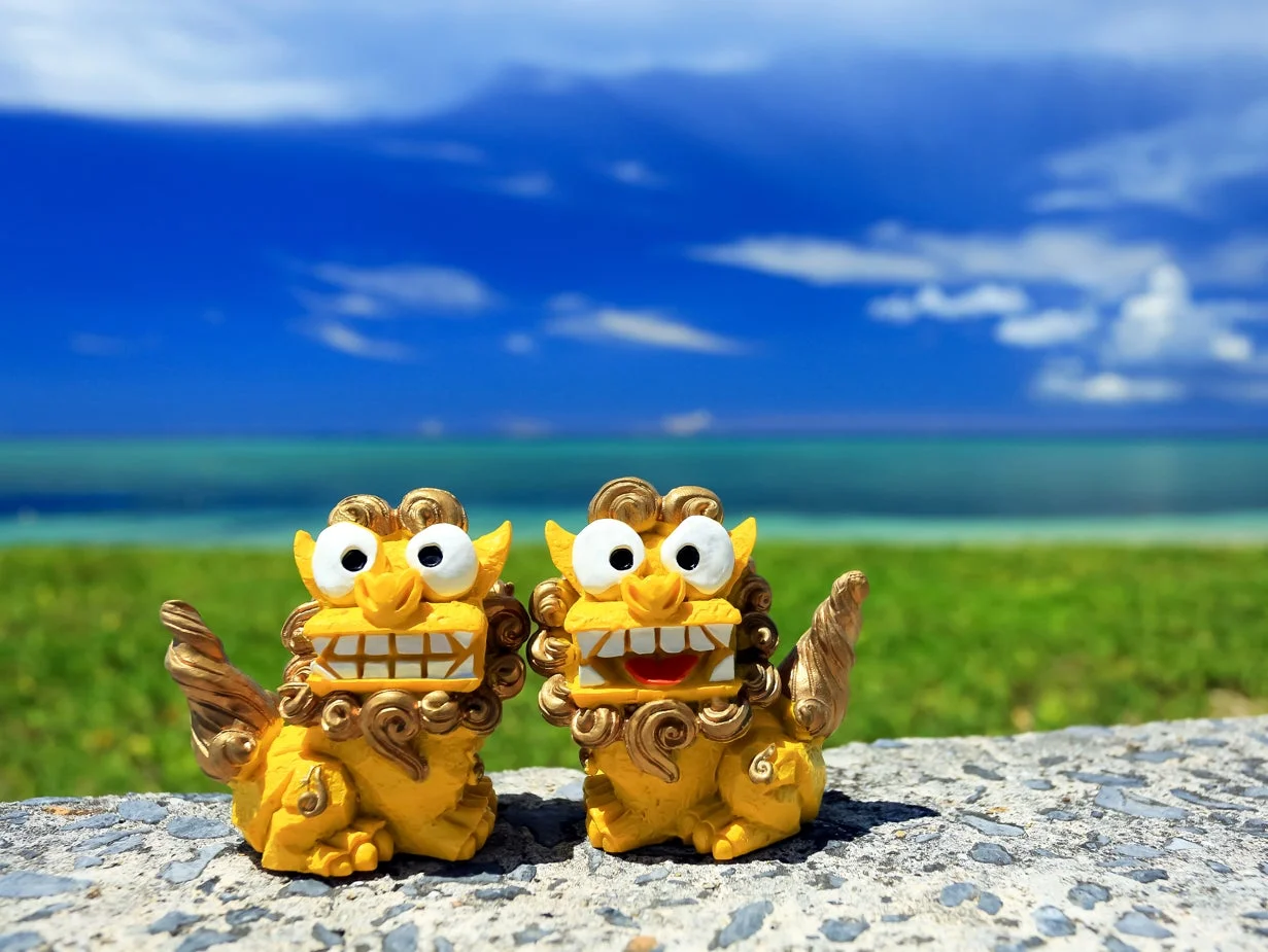 沖縄の美しい海と青空を背景に、愛らしい2体の黄色いシーサーが並んで座っています。