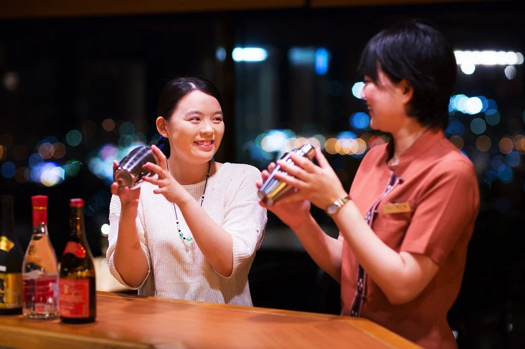 夜景が見えるバーカウンターでカクテルを作る女性たち