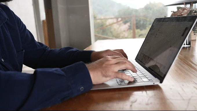 屋内で一人の人物がラップトップのキーボードを操作している様子です。