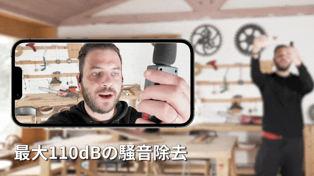 スマートフォン画面にワークショップで作業する男性が映し出され、手にはマイクのようなデバイスを持っている。