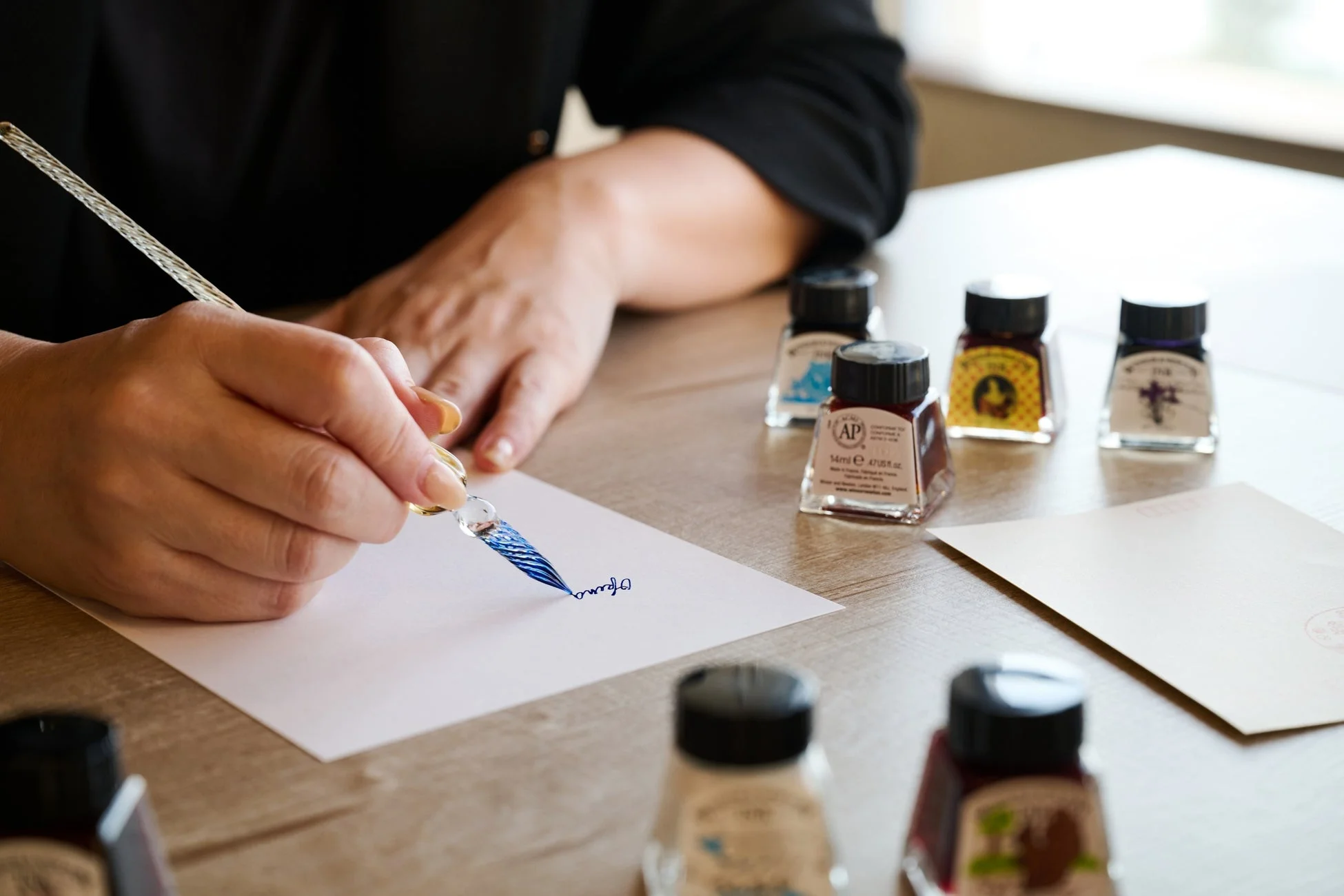 机の上でガラスペンを使い、紙に文字を書いている人物の手元