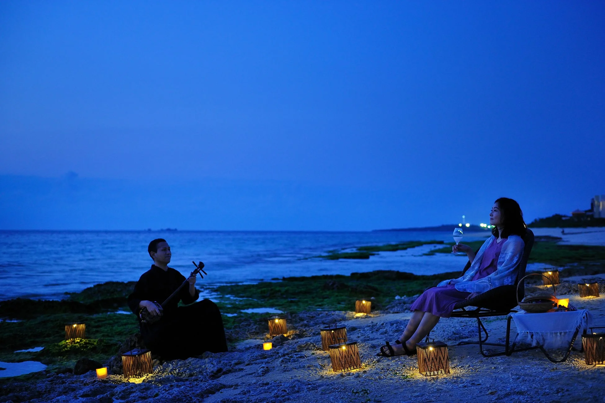 夜のビーチで三線の演奏を聴く女性