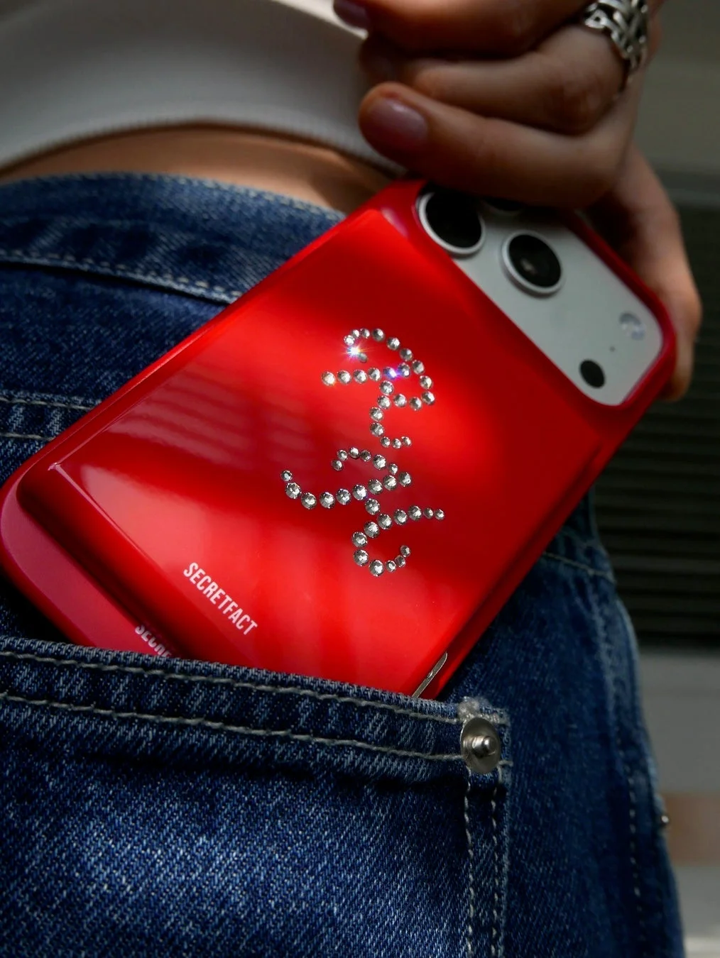 ジーンズのポケットに収まる赤いラインストーンのスマホケース