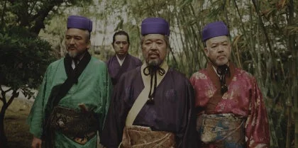 紫色の帽子と伝統的な和服を身につけた4人の男性が屋外を歩いている様子