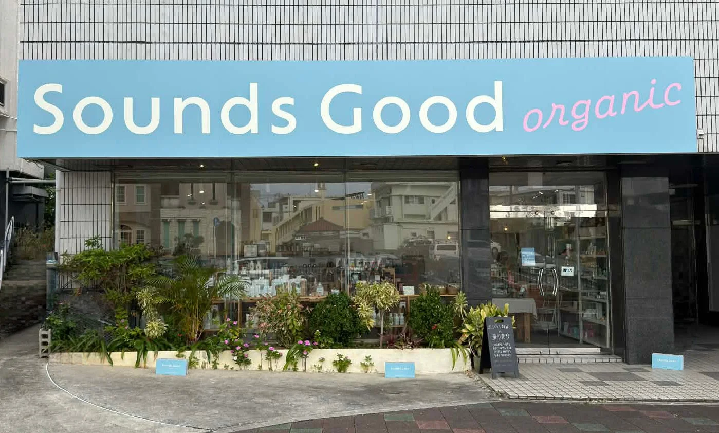 「Sounds Good organic」という看板を掲げた店舗の外観。ガラス張りの店内には商品が並び、店先には緑豊かな植物が飾られています。オーガニック食品や量り売り、エシカル商品を扱うお店のようです。